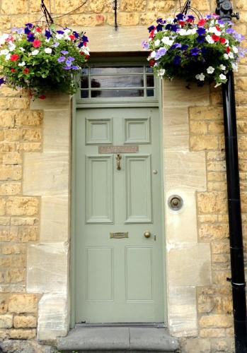 a green door on a stone building with flowers at Chester House Hotel in Bourton on the Water