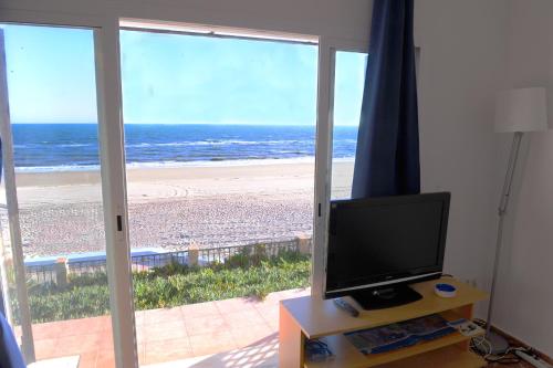a room with a television and a view of a beach at A la Orilla del Mar in Matalascañas