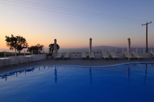 a swimming pool with chairs and a table and the sunset at Maria's Place - Adults Only in Oia