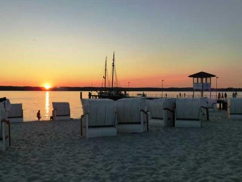 a sunset on the beach with chairs and a boat at Ferienwohnung Strandliebe in Glücksburg