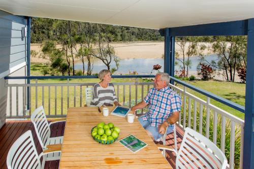 an older man and woman sitting at a table on a porch at Woolgoolga Lakeside Holiday Park in Woolgoolga
