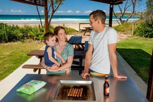 a woman and a man and a child standing at a table at Woolgoolga Lakeside Holiday Park in Woolgoolga