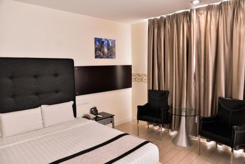 a bedroom with a bed and two black chairs at Shervinton Executive Boutique Hotel in Tawau
