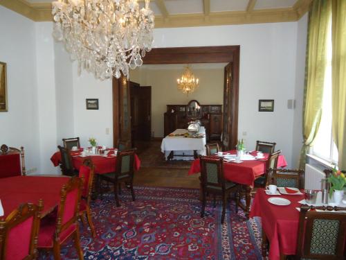 un comedor con mesas y sillas rojas y una lámpara de araña en PP Pension Potsdam, en Potsdam