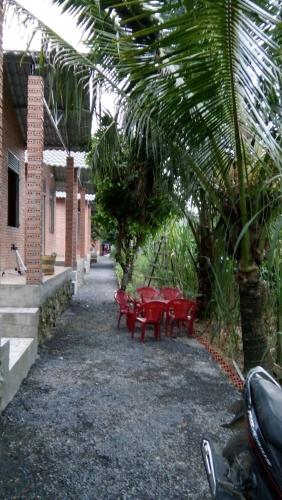 a patio with red tables and chairs and palm trees at Gibbon Singing Home Stay in Quan Tom
