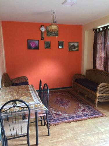 a dining room with orange walls and a table and a couch at Mountside Cottages in Ooty