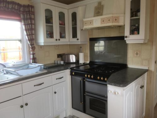 a kitchen with white cabinets and a black stove top oven at Golden palm resort skegness in Chapel Saint Leonards