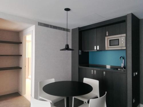 uma cozinha com uma mesa preta e cadeiras brancas em Hg City Suites Barcelona Apartments em Barcelona