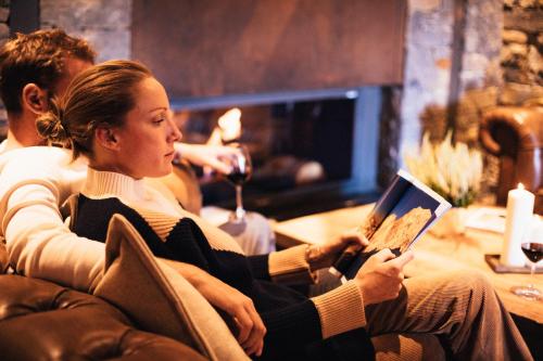 a woman sitting on a couch reading a book at Hôtel L'Arboisie in Megève