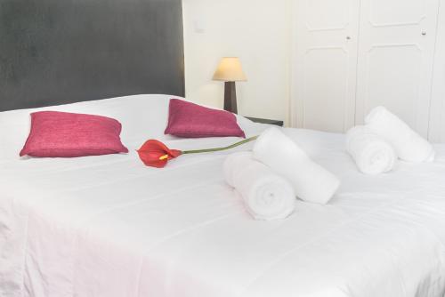a white bed with pink pillows and a red flower on it at Arcadas Cozy Apartments - AU in Funchal