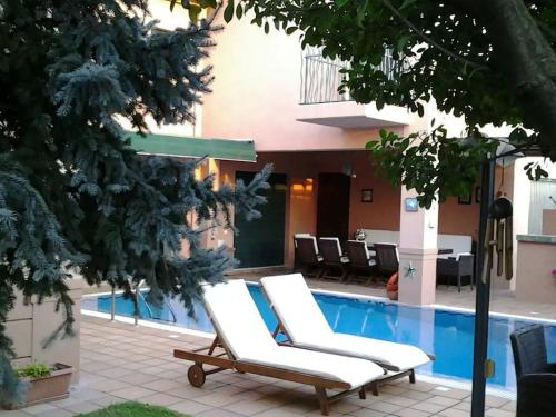 two white lounge chairs next to a swimming pool at 4-seasons pool villa near Meteora in Tríkala