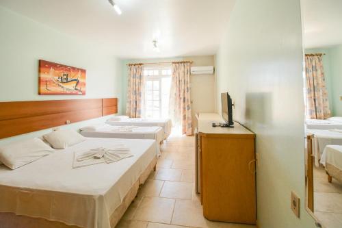 a hotel room with three beds and a television at Pousada Lugar ao Sol in Bombinhas