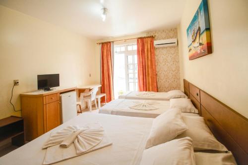 a room with two beds and a desk with a television at Pousada Lugar ao Sol in Bombinhas
