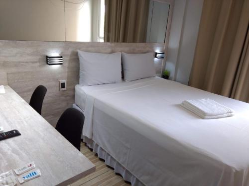 um quarto de hotel com uma grande cama branca e duas mesas em Pertinho do Aeroporto Hospedagem Particular em Várzea Grande