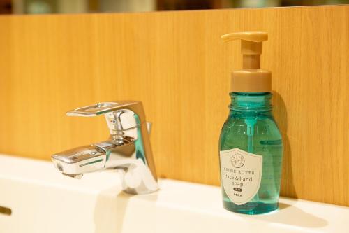 a green bottle of soap sitting on a bathroom sink at Shinjuku Kuyakusho-mae Capsule Hotel in Tokyo