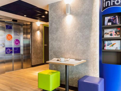 a table and stools in a room with a refrigerator at ibis budget Meudon Paris Ouest in Meudon