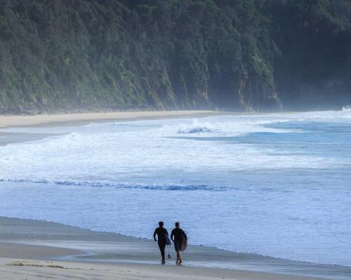 two people walking on the beach with their surfboards at Reflections Seal Rocks - Holiday Park in Smiths Lake