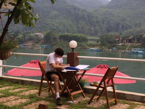 a man sitting at a table next to a lake at Carambola Bungalow in Phong Nha