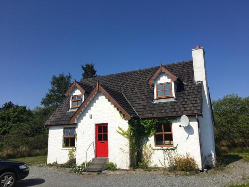 a small white house with a red door at Heatherhill Farm Cottage in Letterfrack beside Connemara National Park in Letterfrack