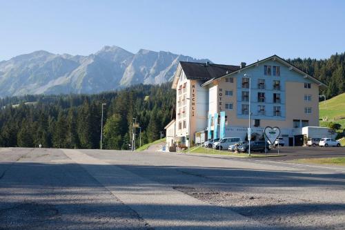 an empty street with a building and mountains in the background at Hotel Rischli in Sörenberg