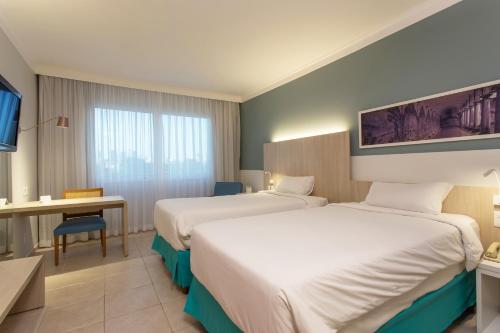 a hotel room with two beds and a desk at Mercure Salvador Rio Vermelho in Salvador