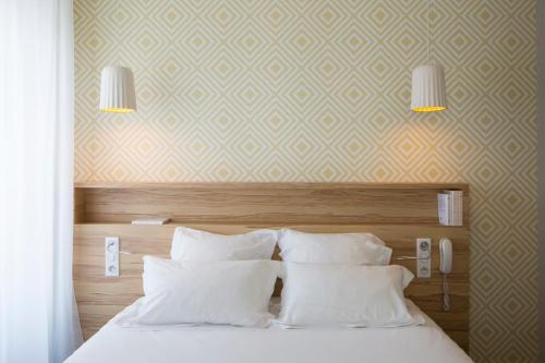 a bedroom with a bed with white pillows and two lights at Hôtel et Apparts Marin in Laval