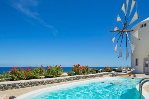 uma piscina com um guarda-sol e o oceano em Windmill Villas em Imerovigli