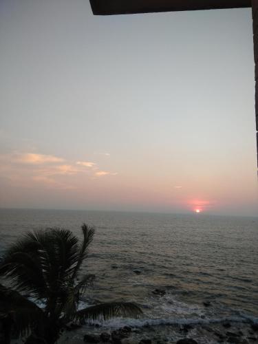 a sunset over the ocean with a palm tree at Om Ganesh Naik Guest House in Arambol