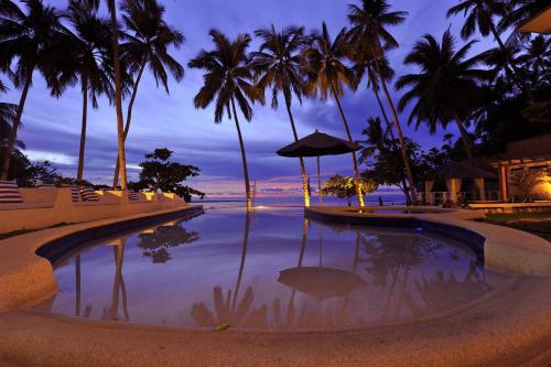 a swimming pool with palm trees and the ocean at night at Punta Bulata White Beach Resort & Spa in Sipalay