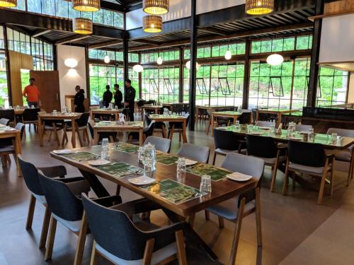 a dining room with tables and chairs and windows at Ayatana Coorg in Somvārpet