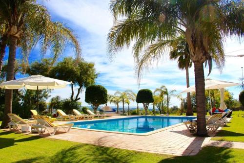 a swimming pool with chairs and umbrellas and palm trees at FARMHOUSE CASA DA AVÓ in Loulé