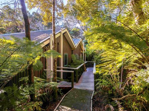 a wooden walkway leading to a house in a forest at Grand Mercure Puka Park Resort in Pauanui