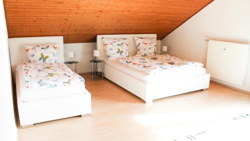 two white beds in a room with wooden ceilings at Ferienwohnung-Fuchs in Bad Schonborn