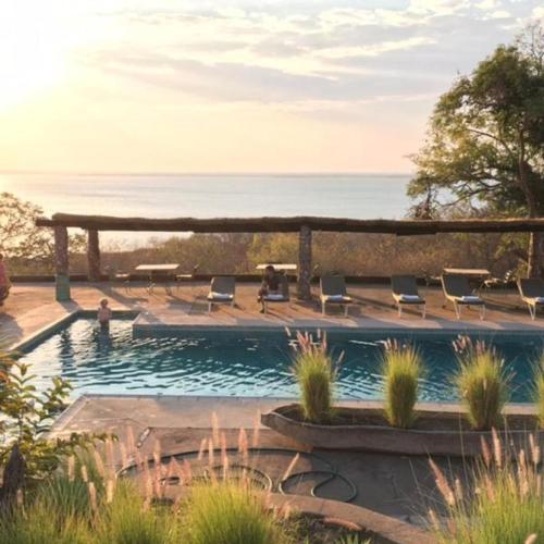 a swimming pool with chairs and the ocean in the background at Musungwa Safari Lodge in Shanjungu