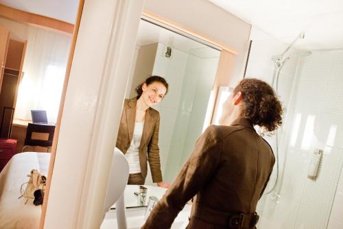 a woman standing in front of a mirror in a bathroom at ibis Lille Centre Gares in Lille