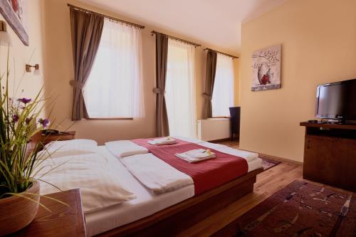 a bedroom with a bed with a red blanket and a television at Hotel Banderium in Komárno