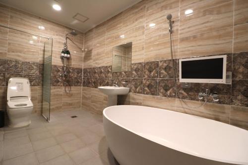 a bathroom with a tub and a toilet and a tv at Hotel Airport in Busan