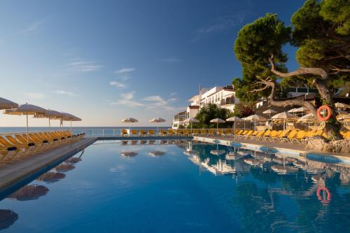 uma piscina ao lado da praia com cadeiras e guarda-sóis em htop Caleta Palace #htopBliss em Platja d'Aro
