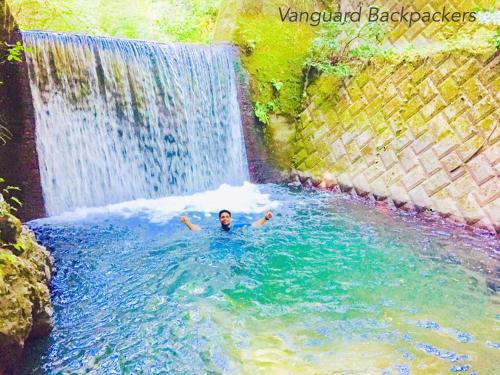 a man swimming in a pool in front of a waterfall at Vanguard Backpackers in Sagamihara