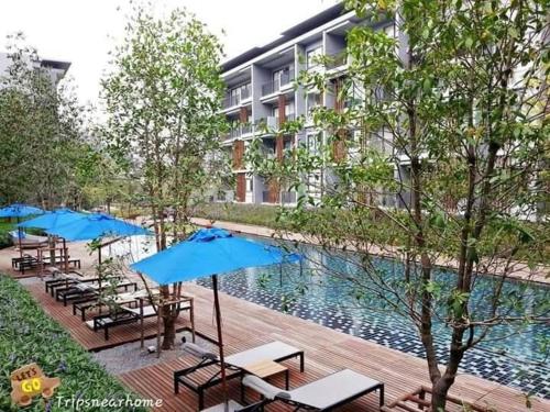 una piscina con mesas y sombrillas junto a un edificio en 23 องศา คอนโด เขาใหญ่ en Nakhon Ratchasima