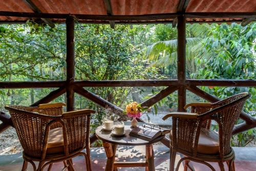 einen Tisch und Stühle auf einer Veranda mit Blick auf die Bäume in der Unterkunft Sunderban Tiger Camp in Gosāba