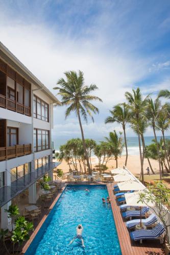 a hotel pool with chairs and a beach at Lucky Elephant Hotel in Hikkaduwa