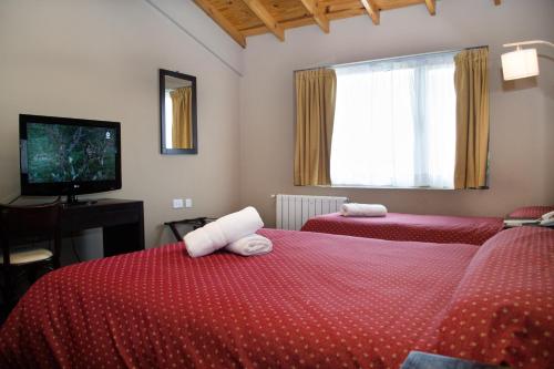 a bedroom with two beds with red sheets and a television at Marcopolo Suites Calafate in El Calafate