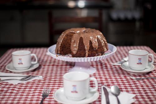 a chocolate cake on a plate on a table with cups at Assay Plaza Hotel in Hortolândia