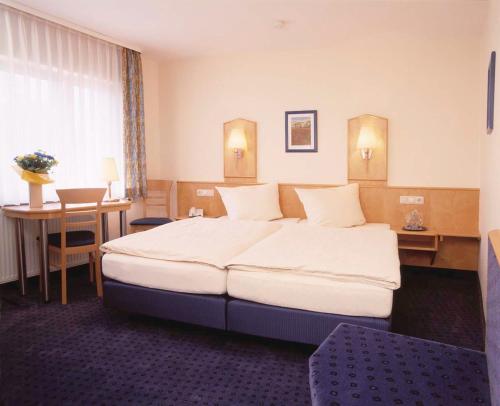 a hotel room with a large bed and a desk at Hotel Sauer Garni in Neu Isenburg