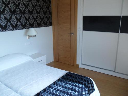 a bedroom with a white bed and a refrigerator at Apartamentos Turisticos Estrella del Alemar in Langre