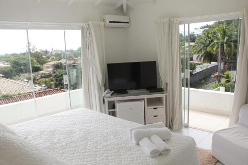een witte slaapkamer met een tv en een bed met handdoeken bij Pousada Solar da Ferradurinha in Búzios