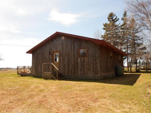 a wooden barn with a red roof in a field at Shaw's Hotel & Cottages in Brackley Beach