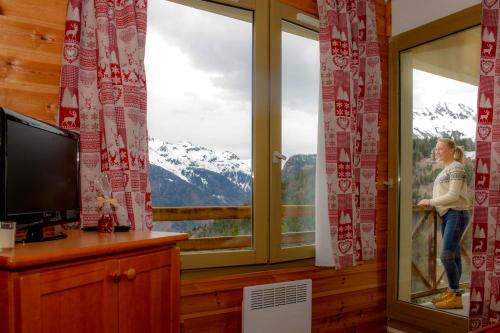 
a woman standing in front of a window looking at a tv at Résidence Couleurs Soleil, Oz en Oisans in Oz
