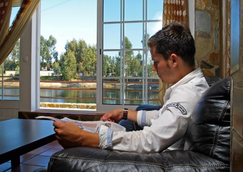a man sitting in a chair looking at his cell phone at Herdade do Sardanito da Frente in Zambujeira do Mar